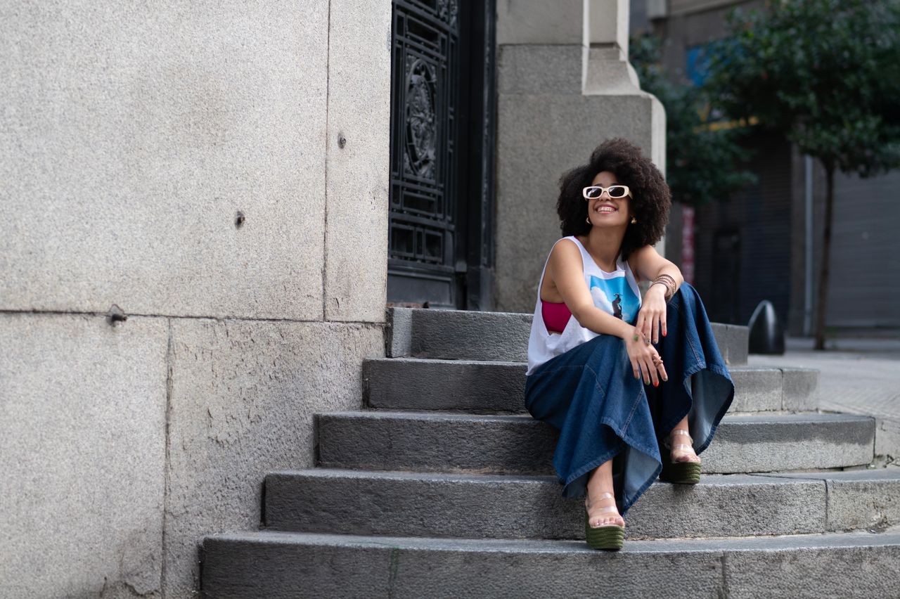 Young woman in stylish attire sitting on steps in Buenos Aires on a sunny day.