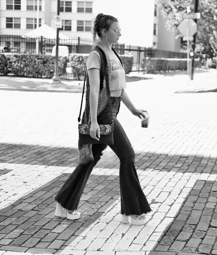 A trendy woman walks confidently with a drink in hand, showcasing her chic fashion sense.